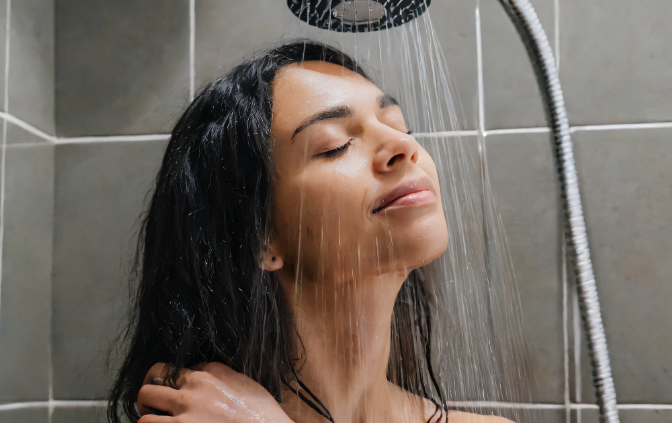 A woman is standing under the shower, she has a relaxed look on her face.